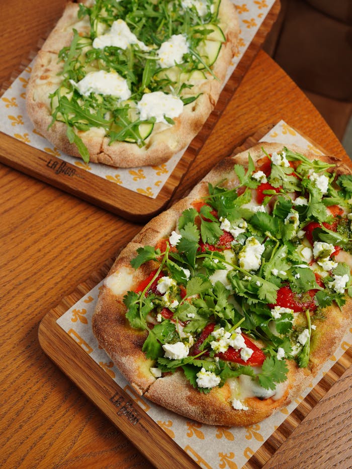Delicious Italian flatbreads with fresh arugula and ricotta on wooden boards.